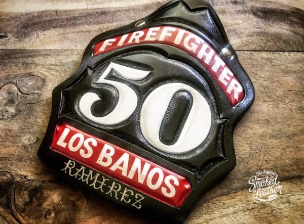 A hard-carved and hand-painted fire helmet shield by Smoked Leather.