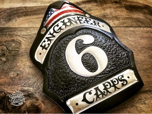 A hard-carved and hand-painted fire helmet shield by Smoked Leather.