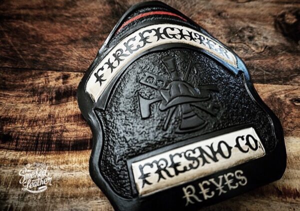 A hard-carved and hand-painted fire helmet shield by Smoked Leather.