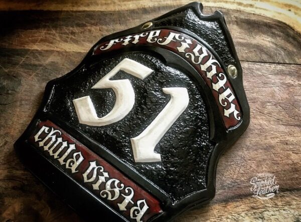 A hard-carved and hand-painted fire helmet shield by Smoked Leather.